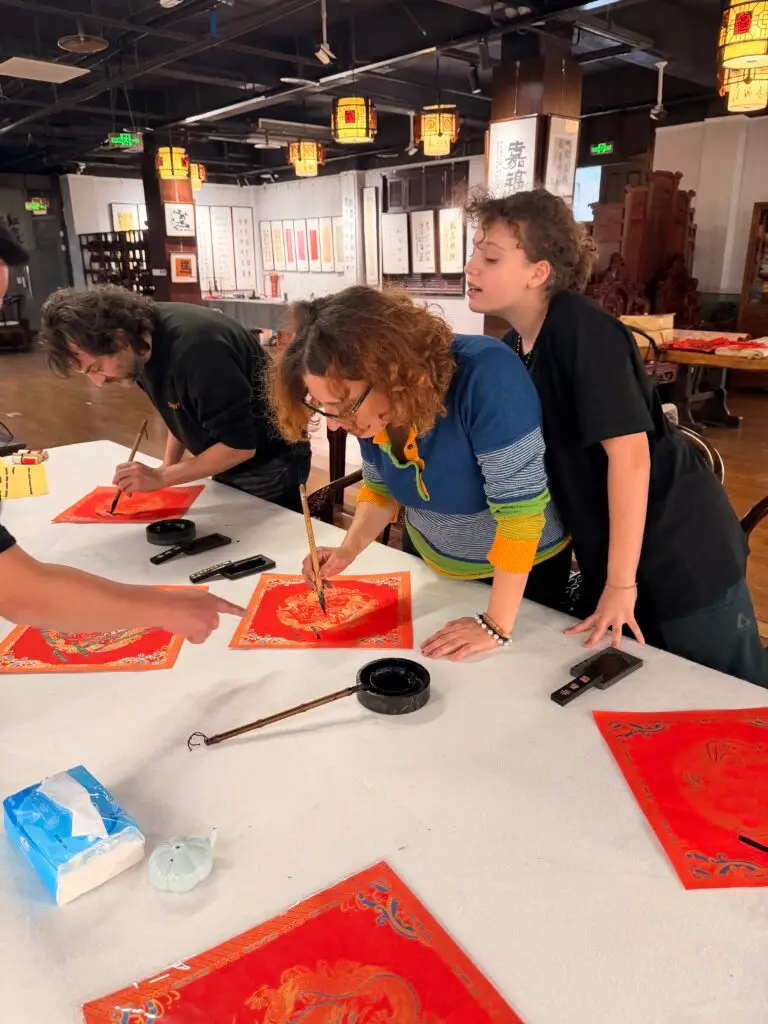 Guests practicing Chinese calligraphy with brush and ink on rice paper, creating handmade artwork to take home as souvenirs
