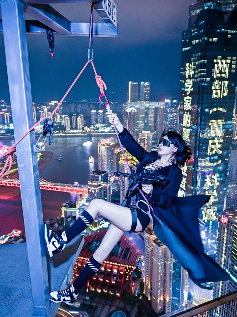 Cyberpunk photography from the Hanging Realm session featuring a woman in techwear rappelling off a Chongqing skyscraper at night with neon city lights.