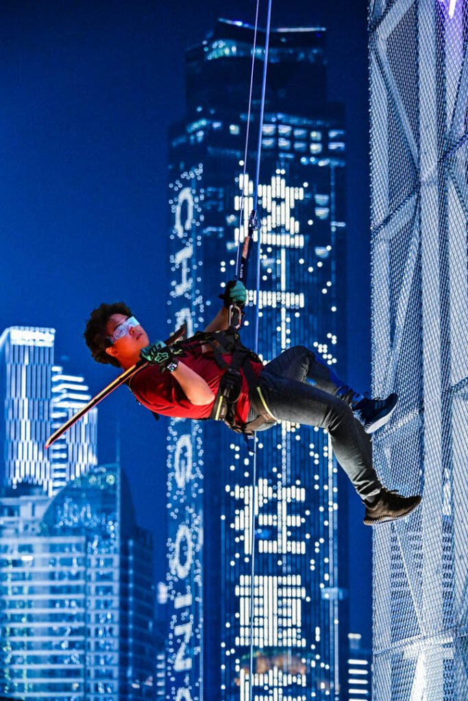 A person in a Blade Runner-style pose rappelling high above the Chongqing cyberpunk city skyline, creating a gravity-defying, 'flying on buildings' effect